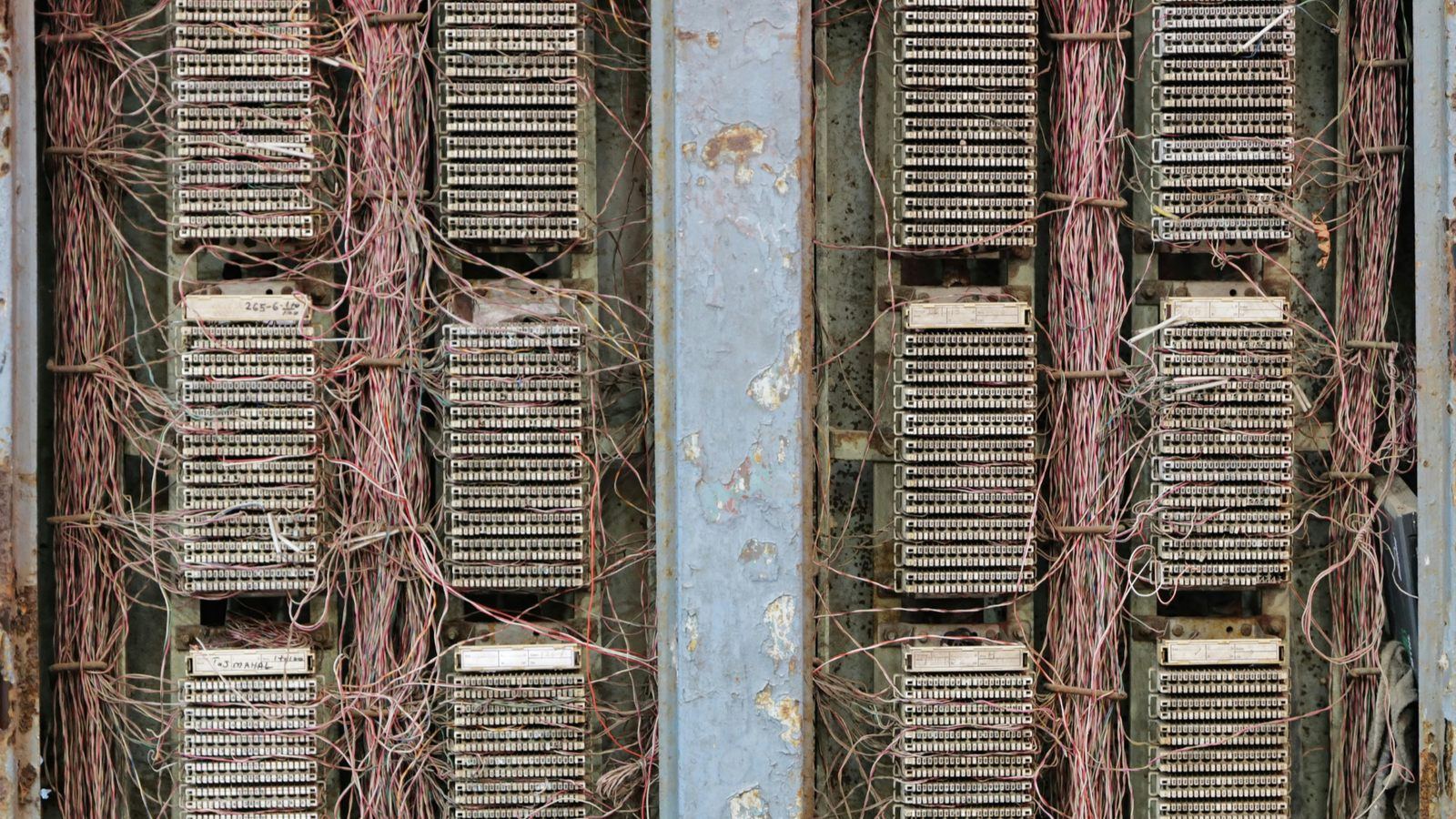 Rows of old copper telephone terminal blocks on a wall, with decades of wiring running into them