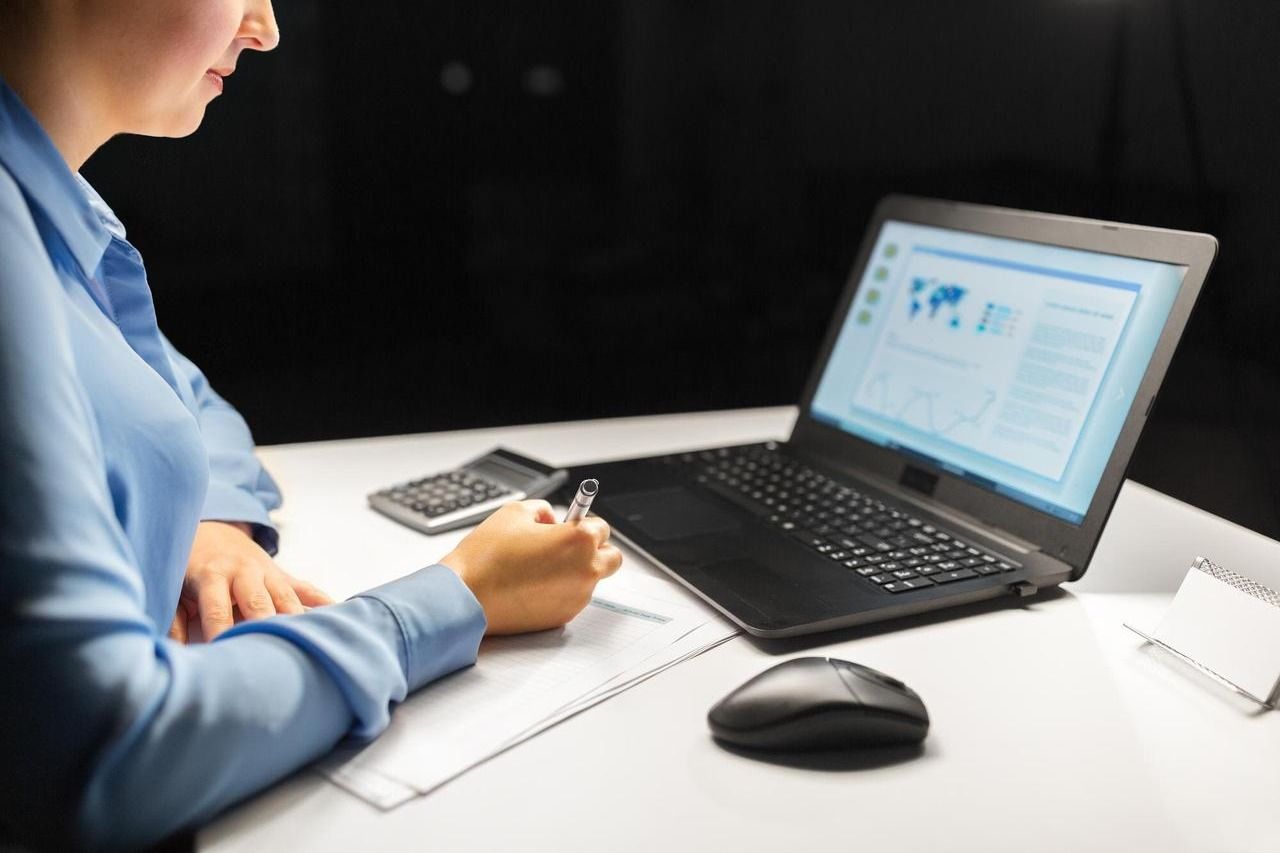 Hands filling in a budget worksheet beside a laptop